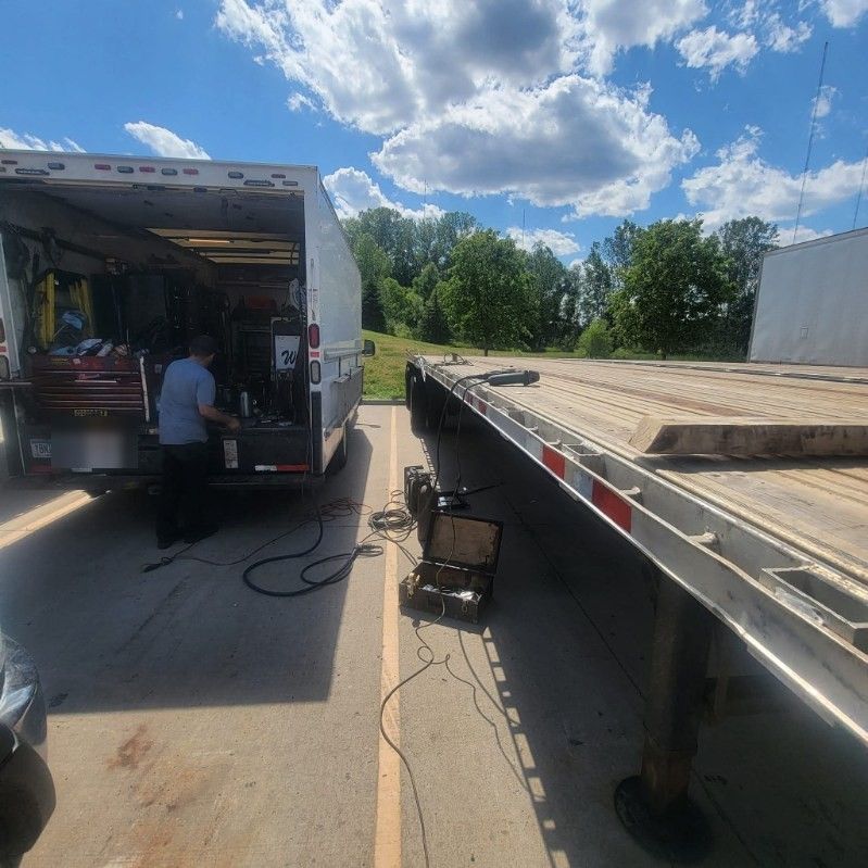 Mobile mechanic working from a fully stocked service truck beside a flatbed trailer