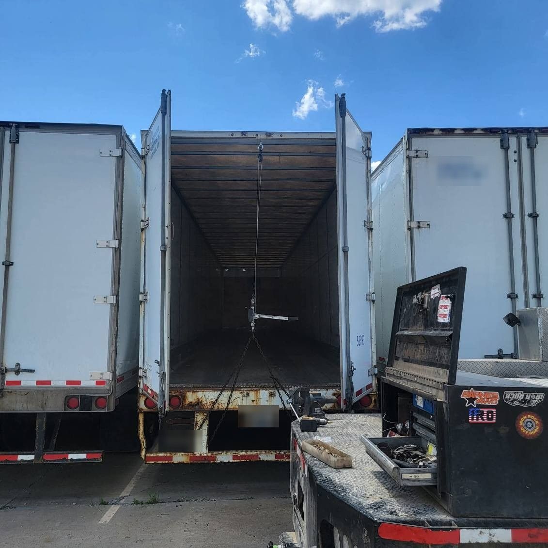 Reefer trailer doors open for repair, service truck parked alongside in the yard